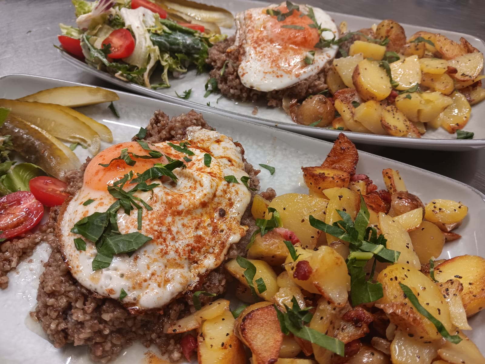 Zwei Teller mit Bratkartoffeln, gebratenem Ei, Hackfleisch, Salat und Gewürzgarnitur