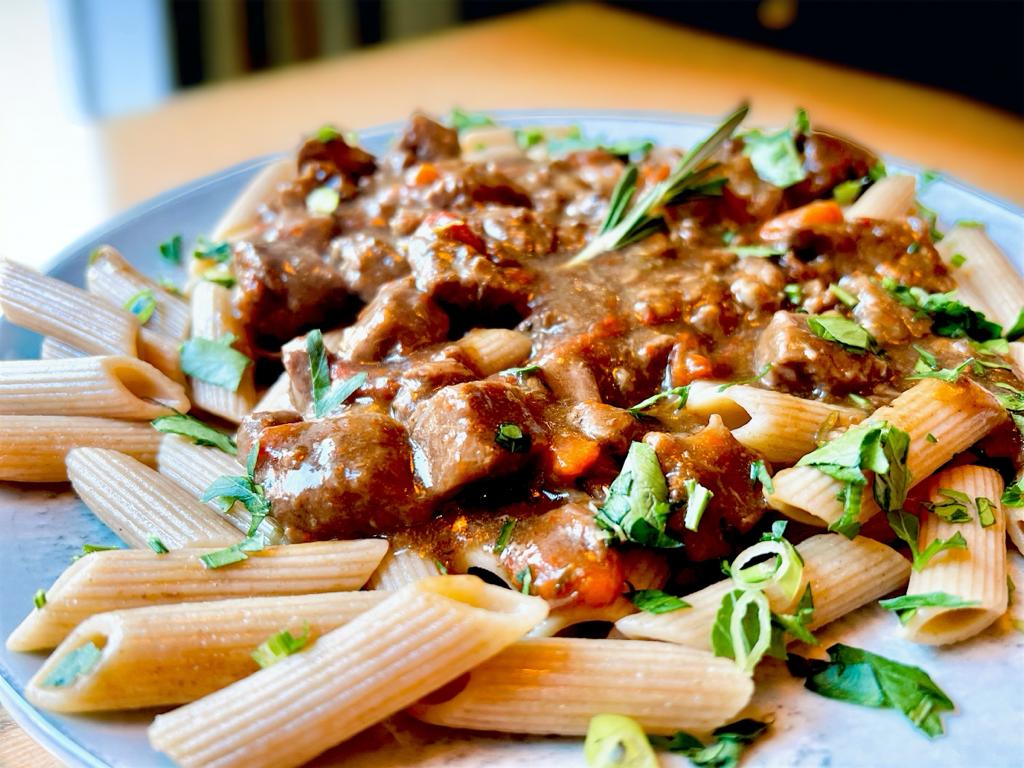 Vollkornnudeln mit dunklem Rinder-Ragout und frischen Kräutern angerichtet