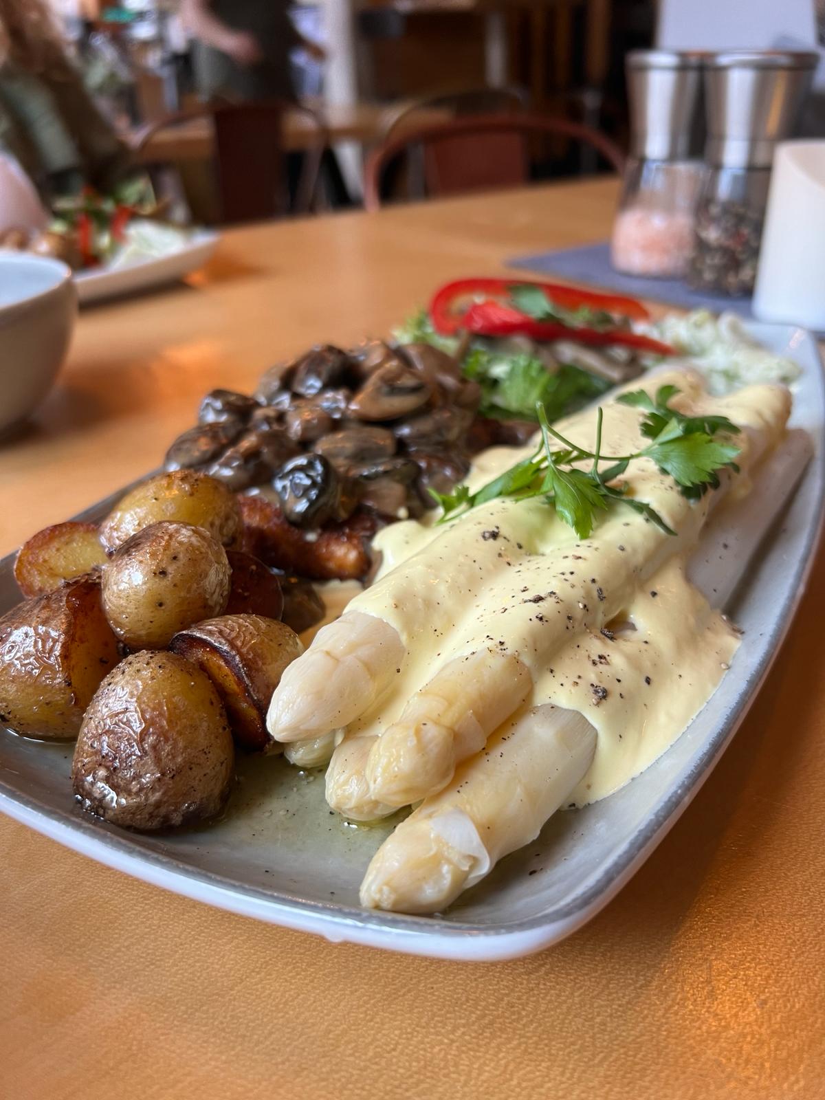 Weißer Spargel mit Kartoffeln, Pilzen und Sauce Hollandaise auf einem weißen Teller
